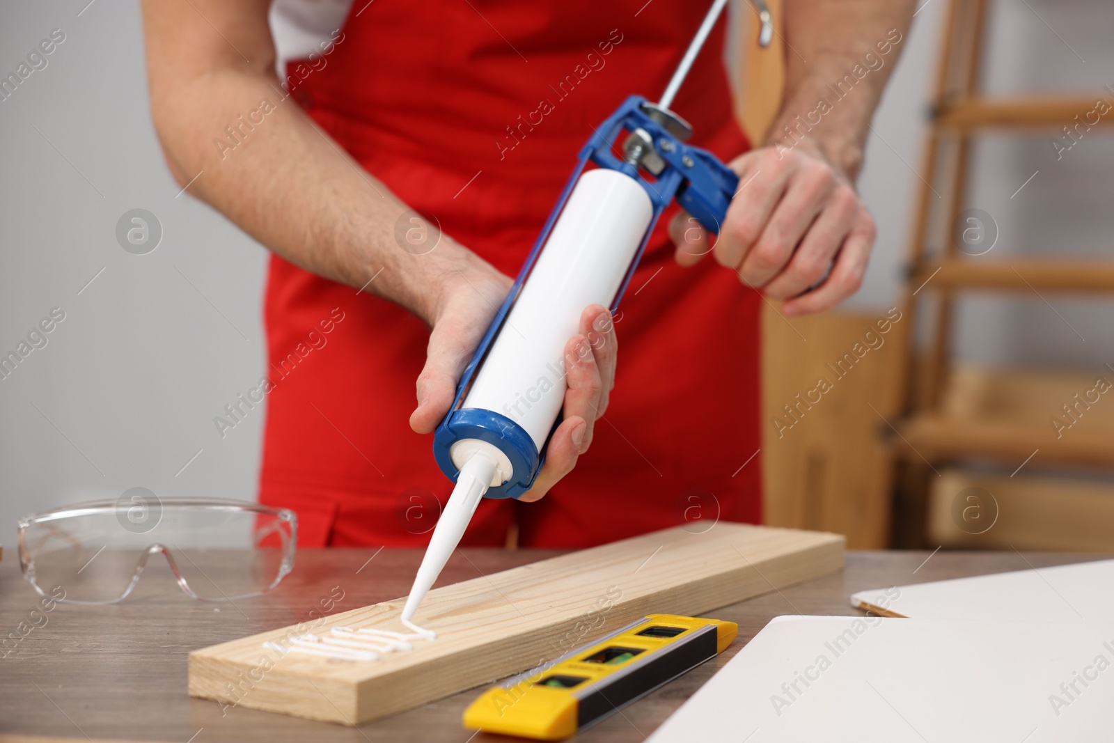 Photo of Worker with caulking gun glueing wooden plank indoors, closeup