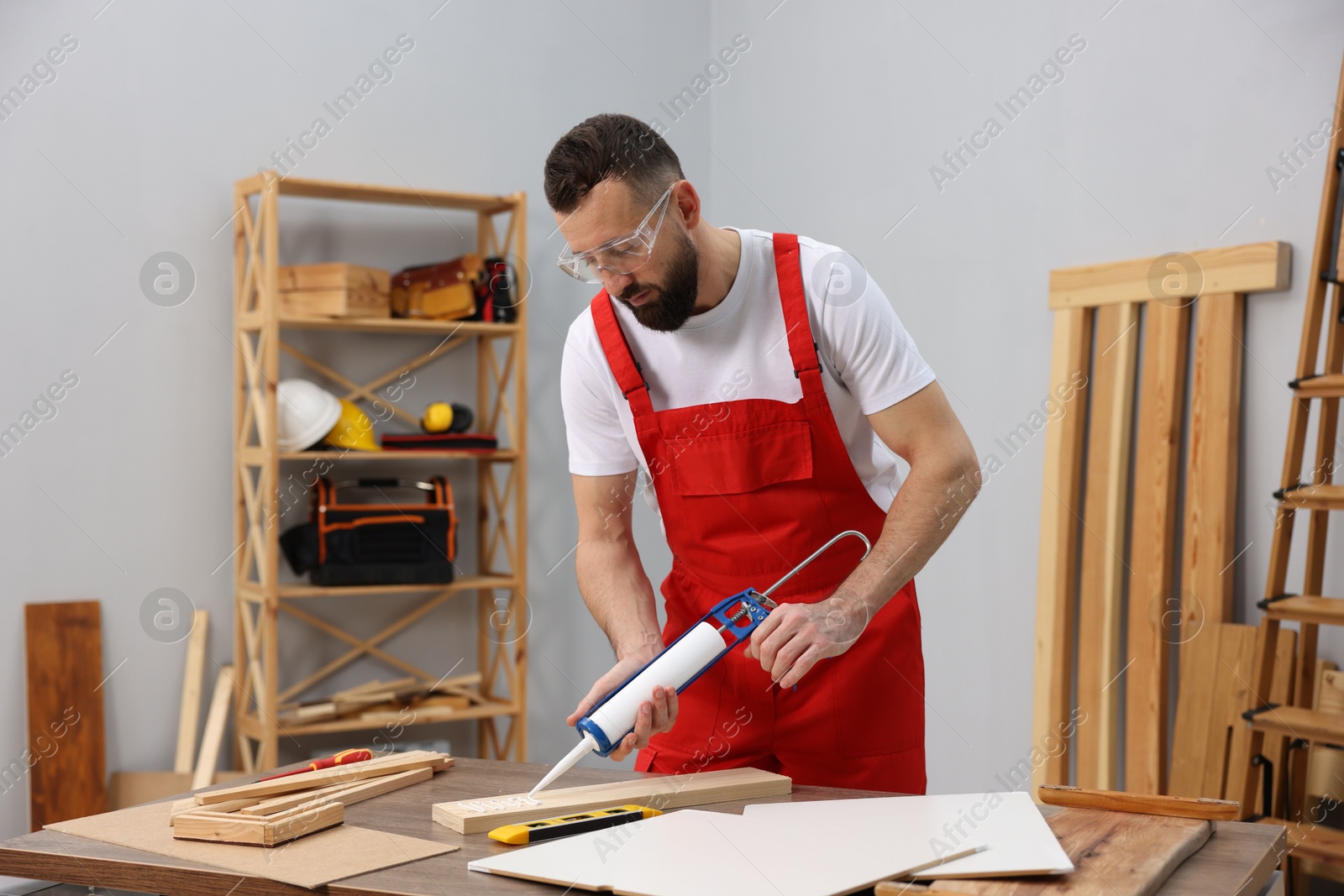 Photo of Worker with caulking gun glueing wooden plank indoors