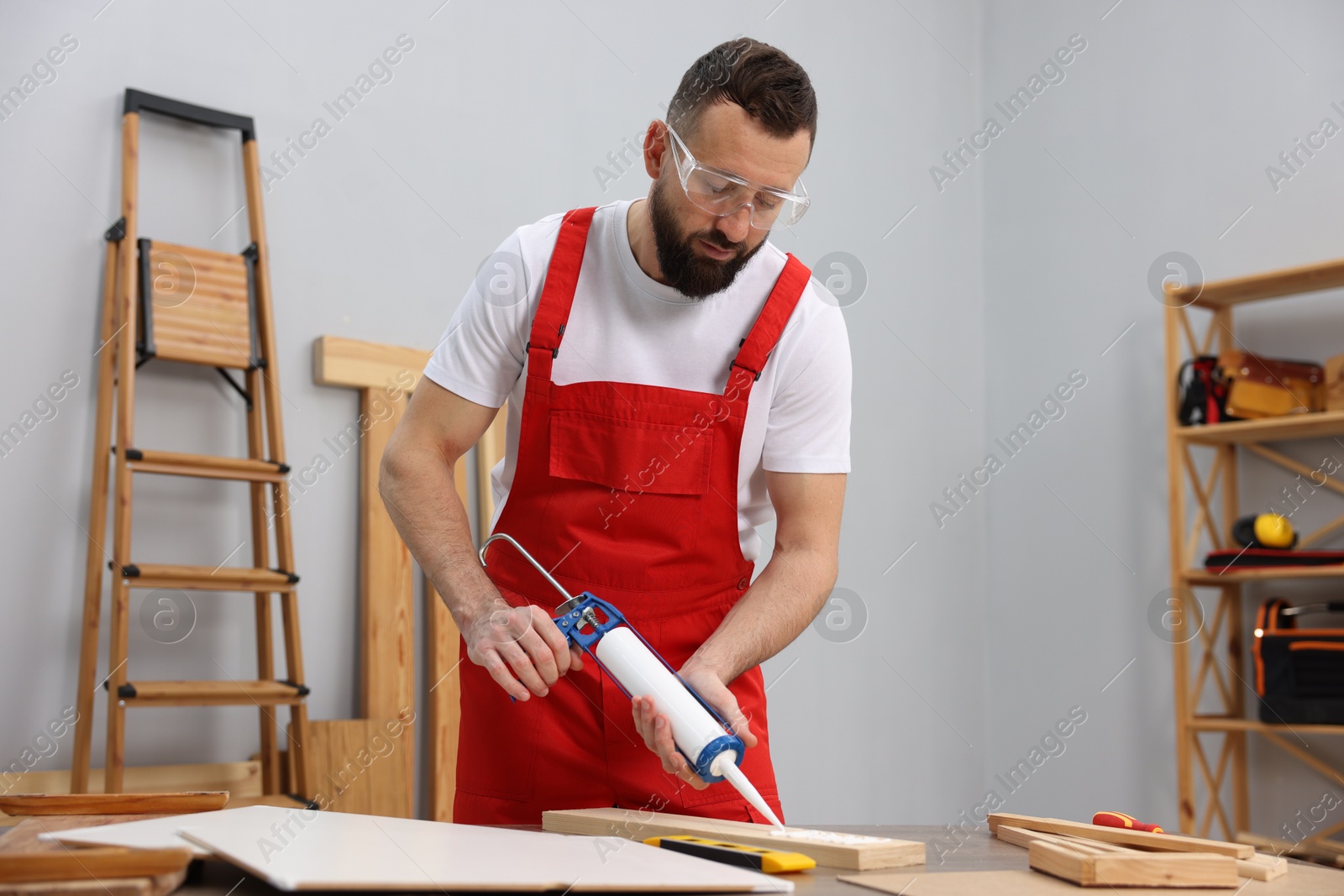 Photo of Worker with caulking gun glueing wooden plank indoors