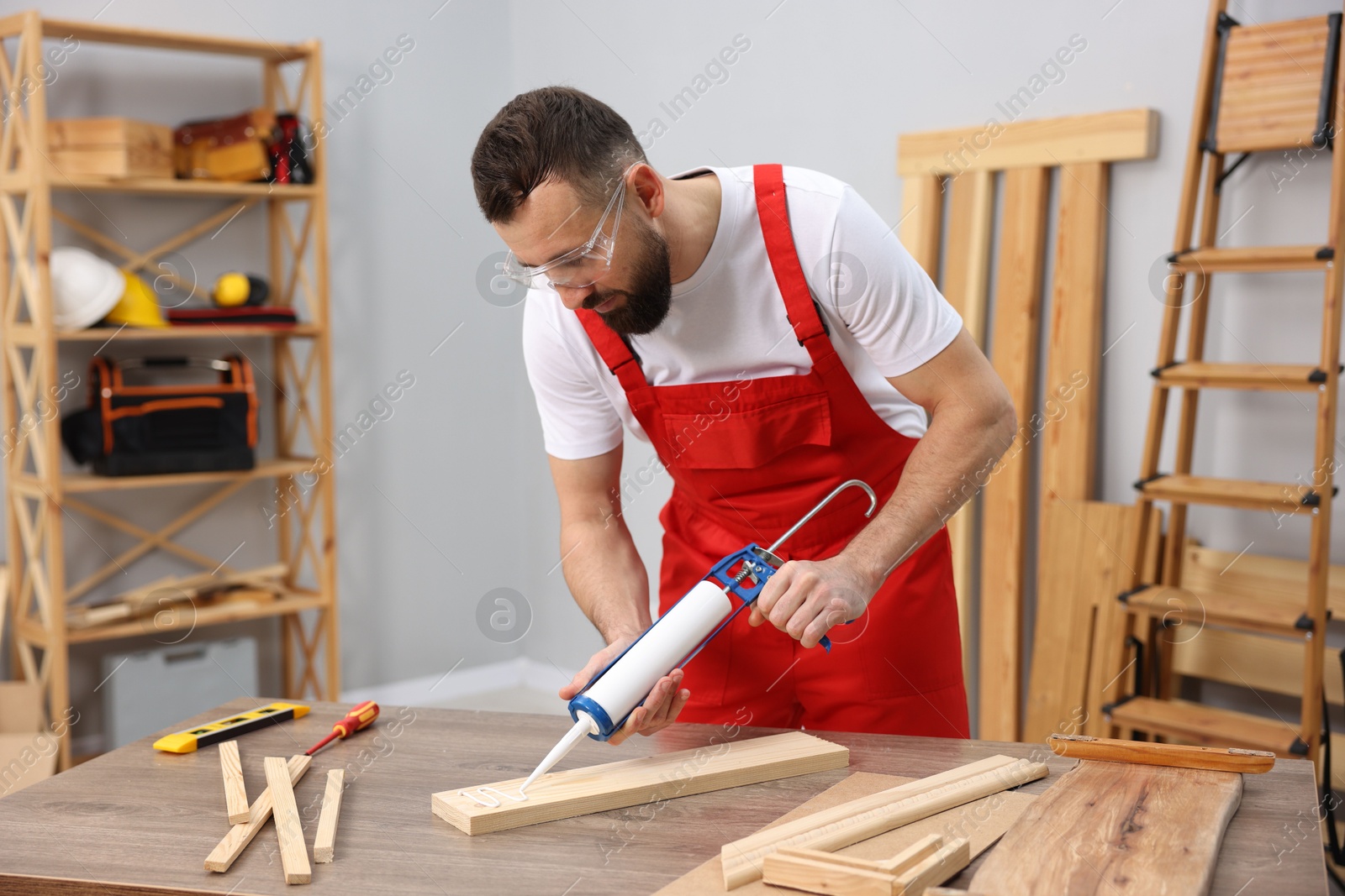 Photo of Worker with caulking gun glueing wooden plank indoors