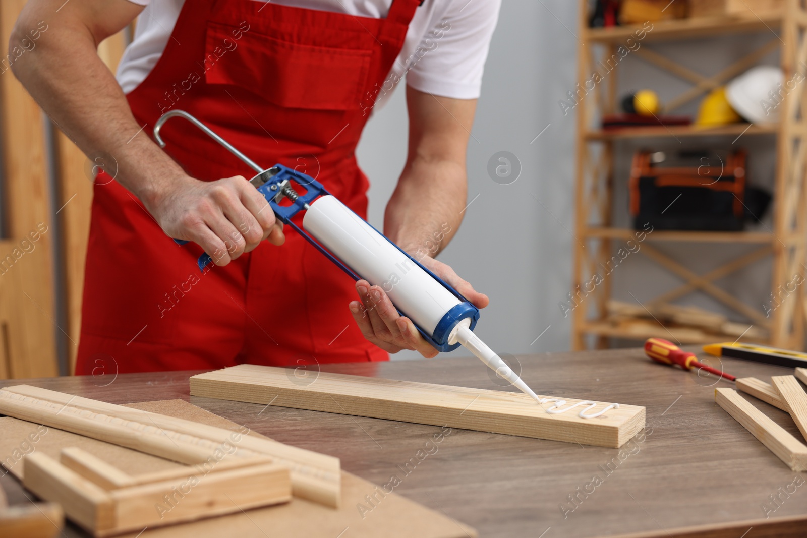 Photo of Worker with caulking gun glueing wooden plank indoors, closeup