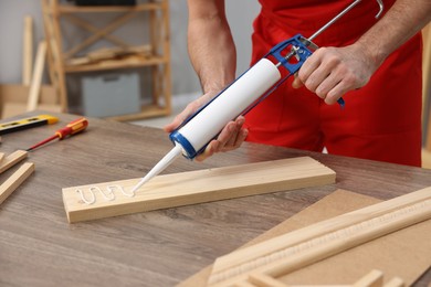 Photo of Worker with caulking gun glueing wooden plank indoors, closeup