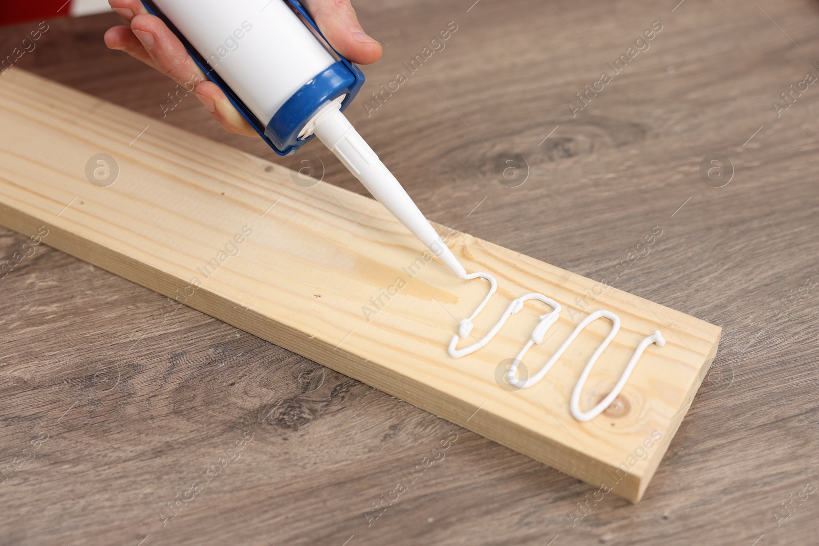 Photo of Man with caulking gun glueing wooden plank at table, closeup