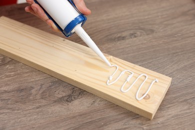 Photo of Man with caulking gun glueing wooden plank at table, closeup