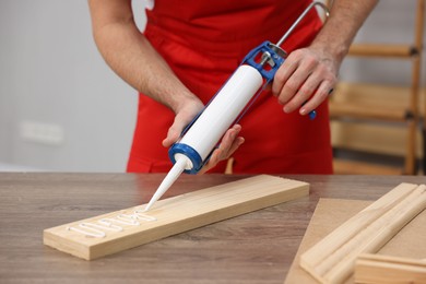 Photo of Worker with caulking gun glueing wooden plank indoors, closeup