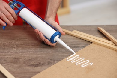 Photo of Man with caulking gun glueing plywood at wooden table, closeup