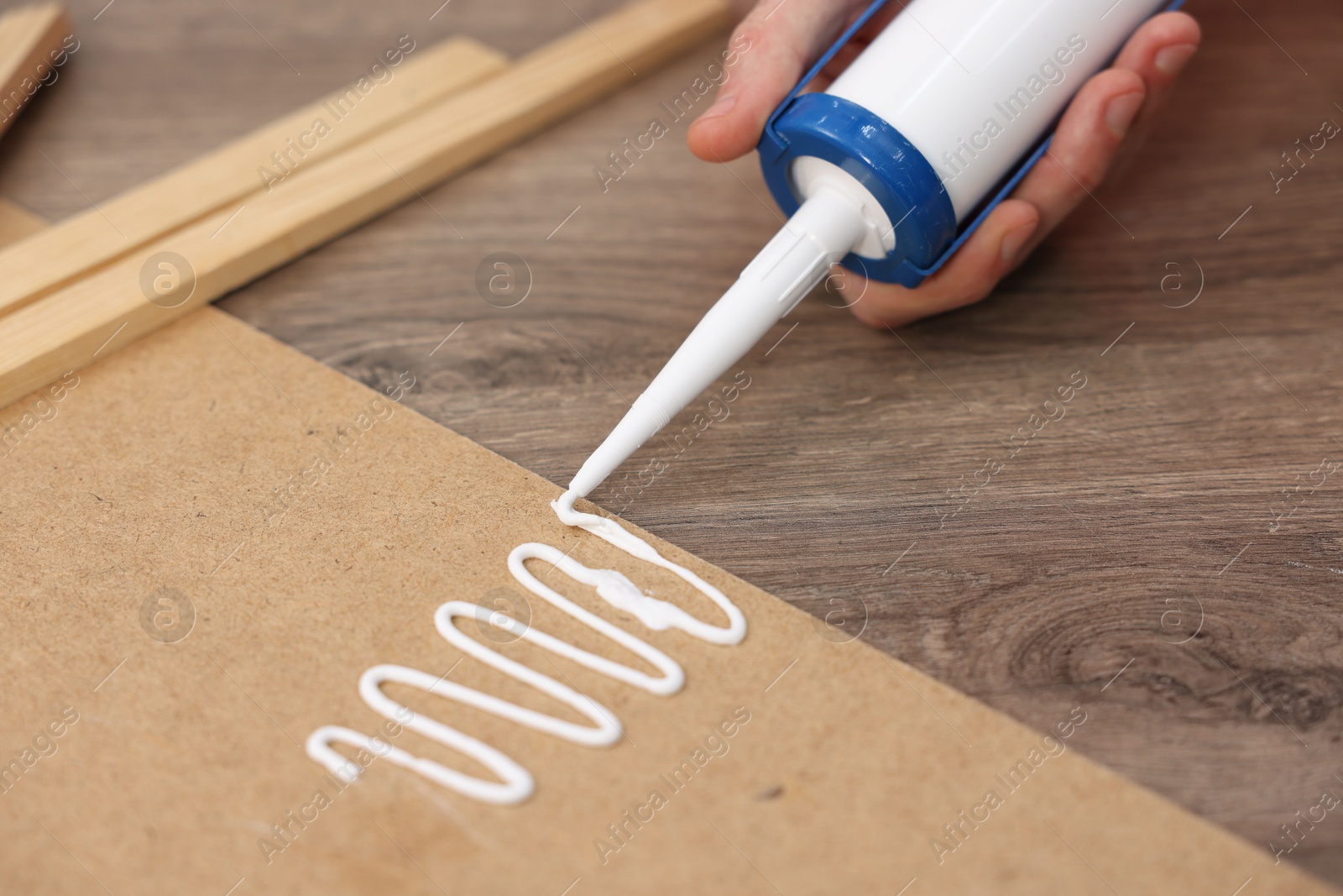 Photo of Man with caulking gun glueing plywood at wooden table, closeup