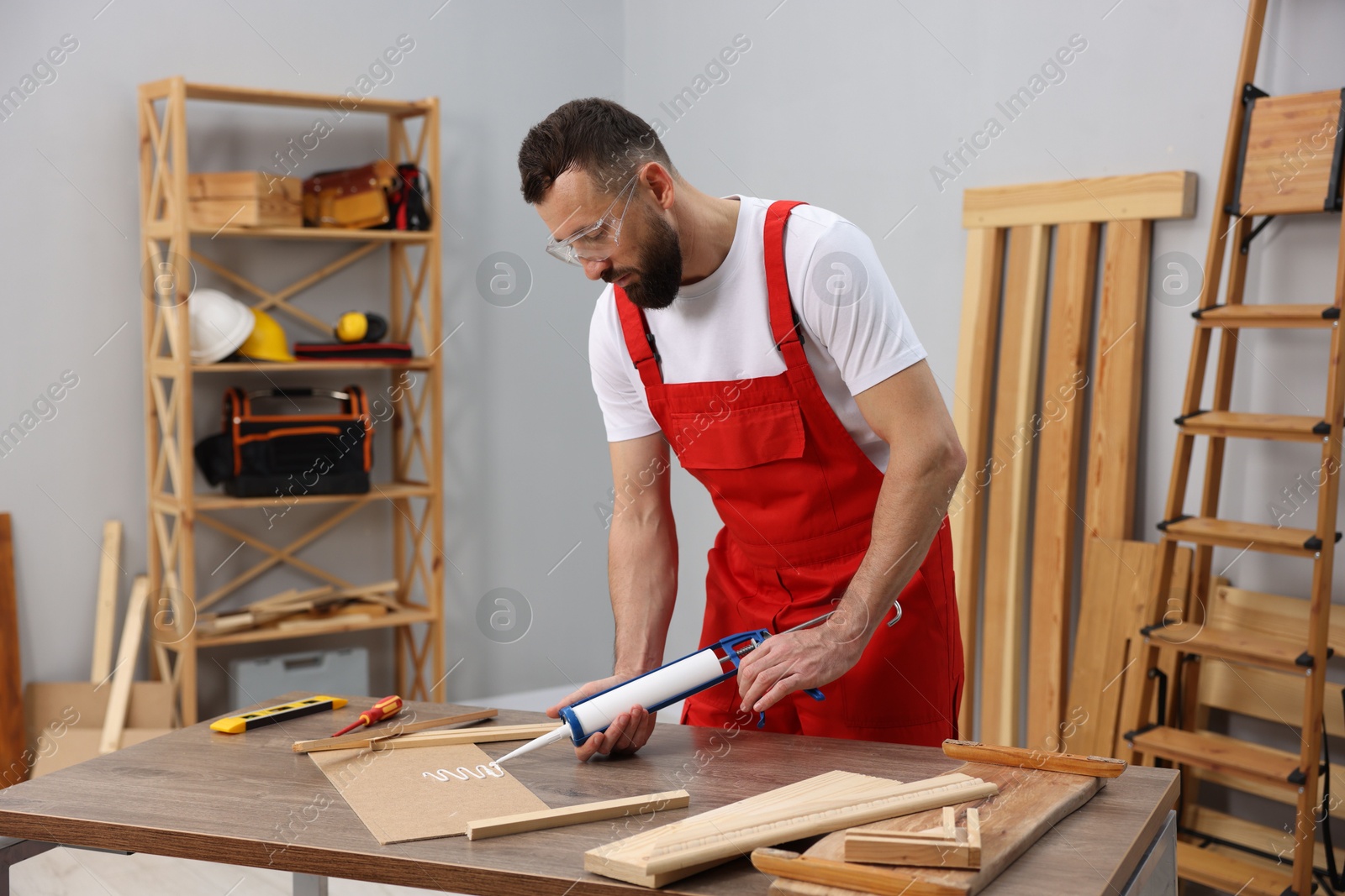 Photo of Worker with caulking gun glueing wooden plank indoors