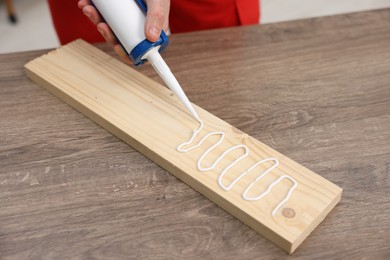 Photo of Man with caulking gun glueing wooden plank at table, closeup