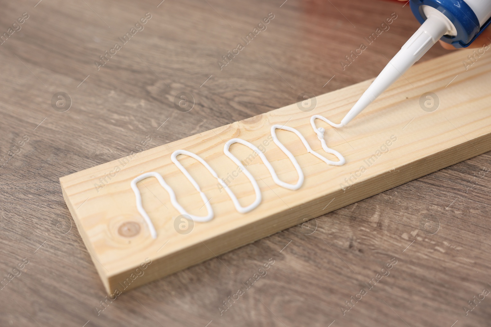 Photo of Man with caulking gun glueing wooden plank at table, closeup