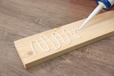 Photo of Man with caulking gun glueing wooden plank at table, closeup