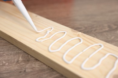 Photo of Man with caulking gun glueing wooden plank at table, closeup