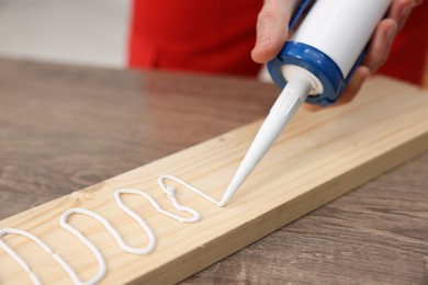 Photo of Man with caulking gun glueing wooden plank at table, closeup