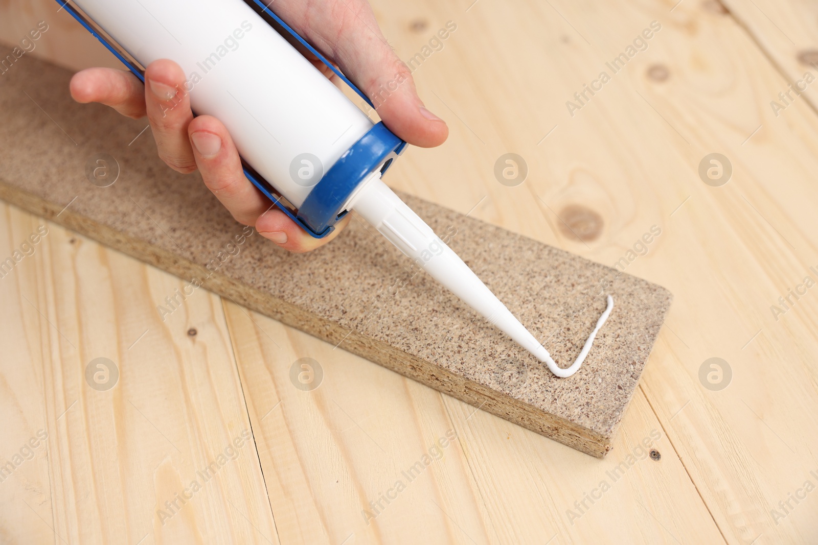 Photo of Man with caulking gun glueing wooden plank at table, closeup