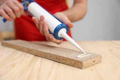 Photo of Man with caulking gun glueing wooden plank at table, closeup