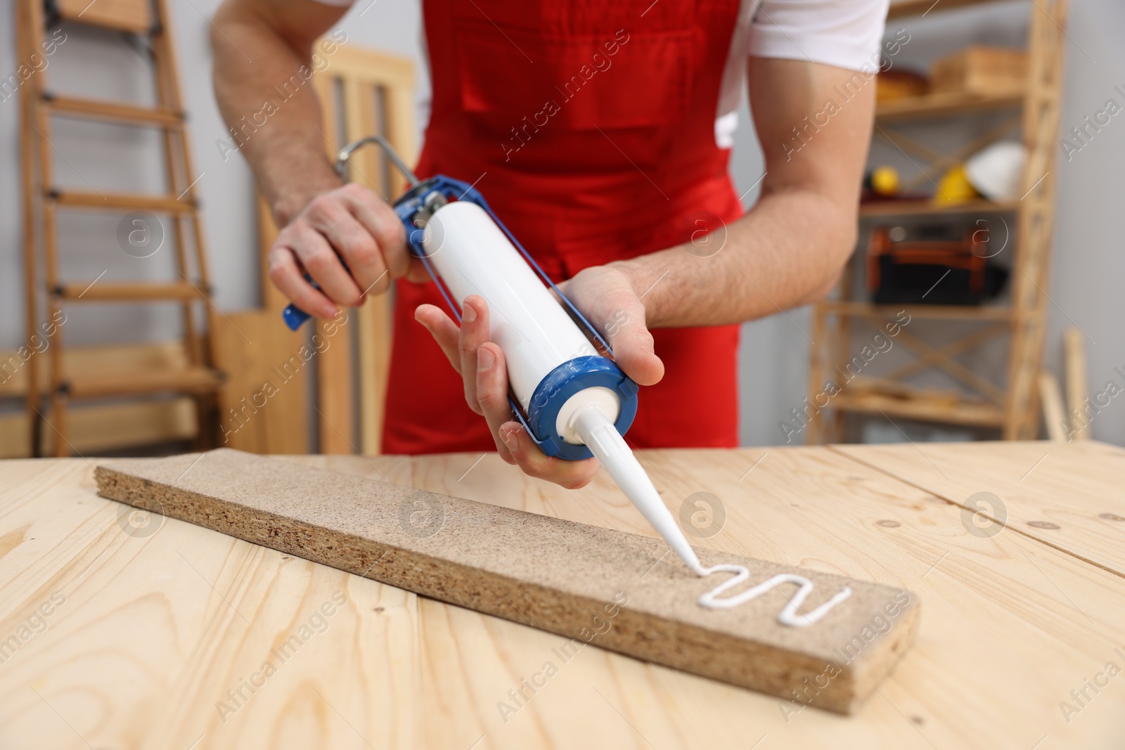 Photo of Worker with caulking gun glueing wooden plank indoors, closeup