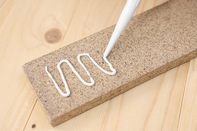 Photo of Glueing wooden plank with caulking gun at table, closeup