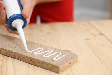 Photo of Man with caulking gun glueing wooden plank at table, closeup