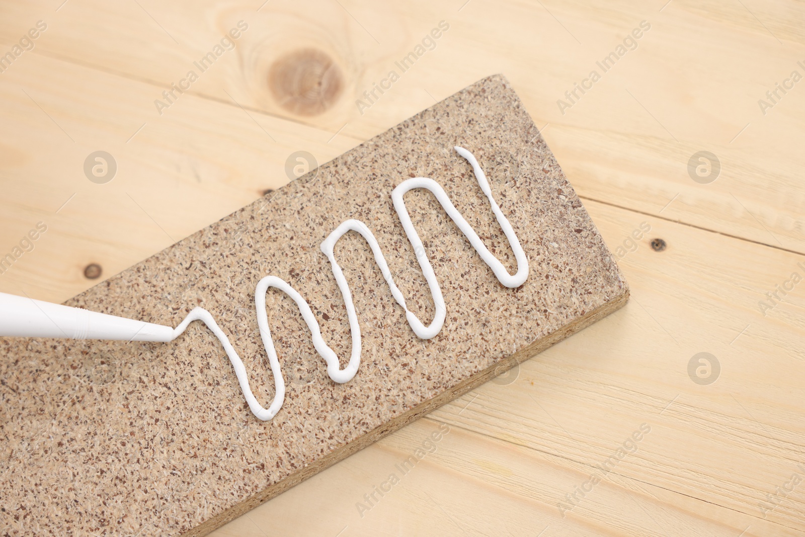 Photo of Glueing wooden plank with caulking gun at table, top view