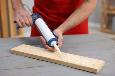 Photo of Worker with caulking gun glueing wooden plank at gray table, closeup