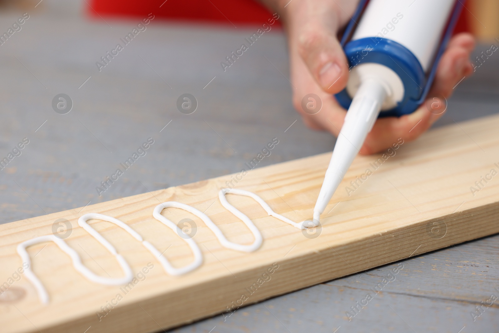 Photo of Man with caulking gun glueing wooden plank at gray table, closeup