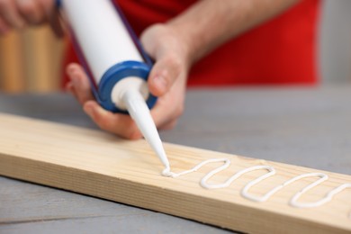 Photo of Man with caulking gun glueing wooden plank at gray table, closeup