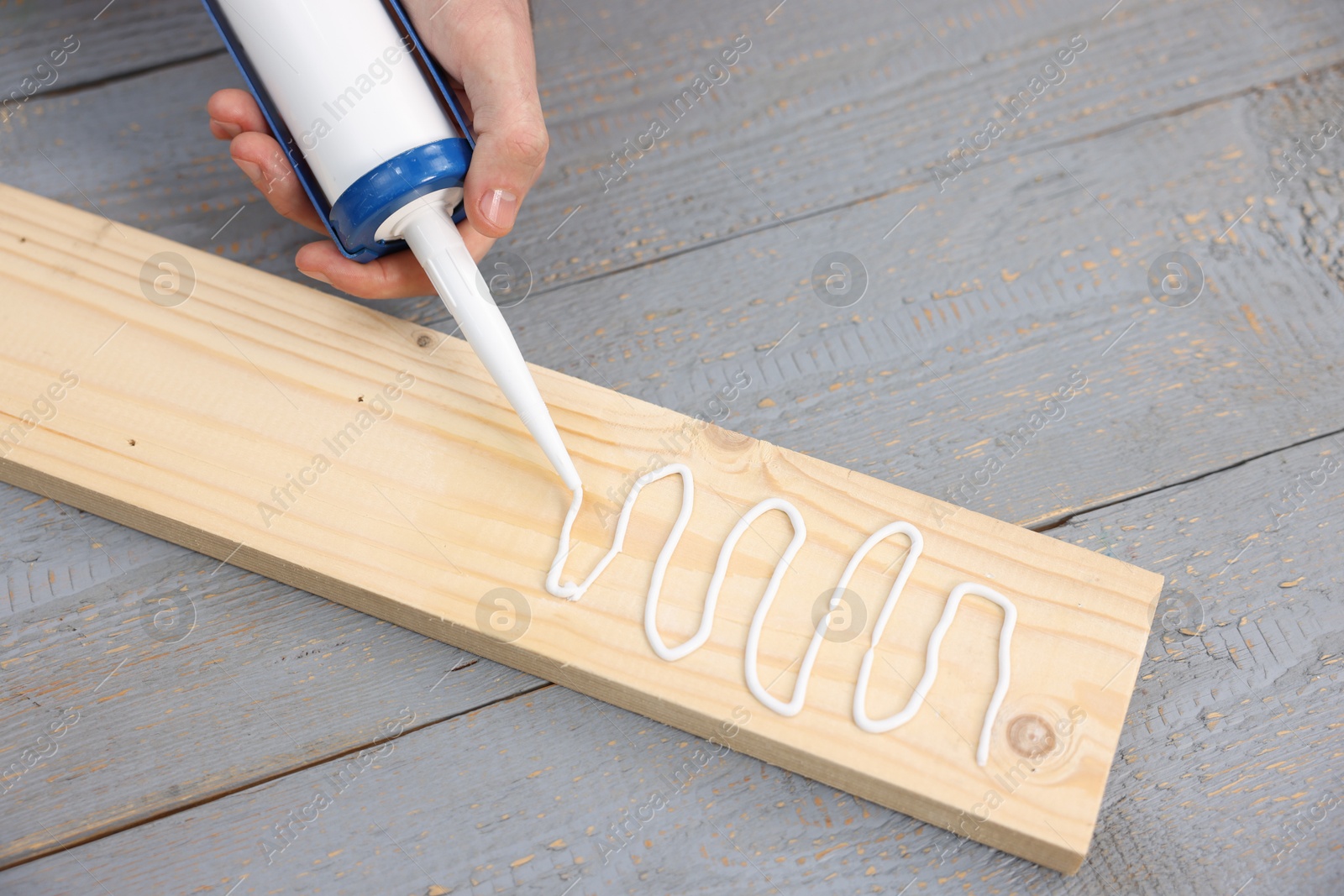 Photo of Man with caulking gun glueing wooden plank at gray table, above view