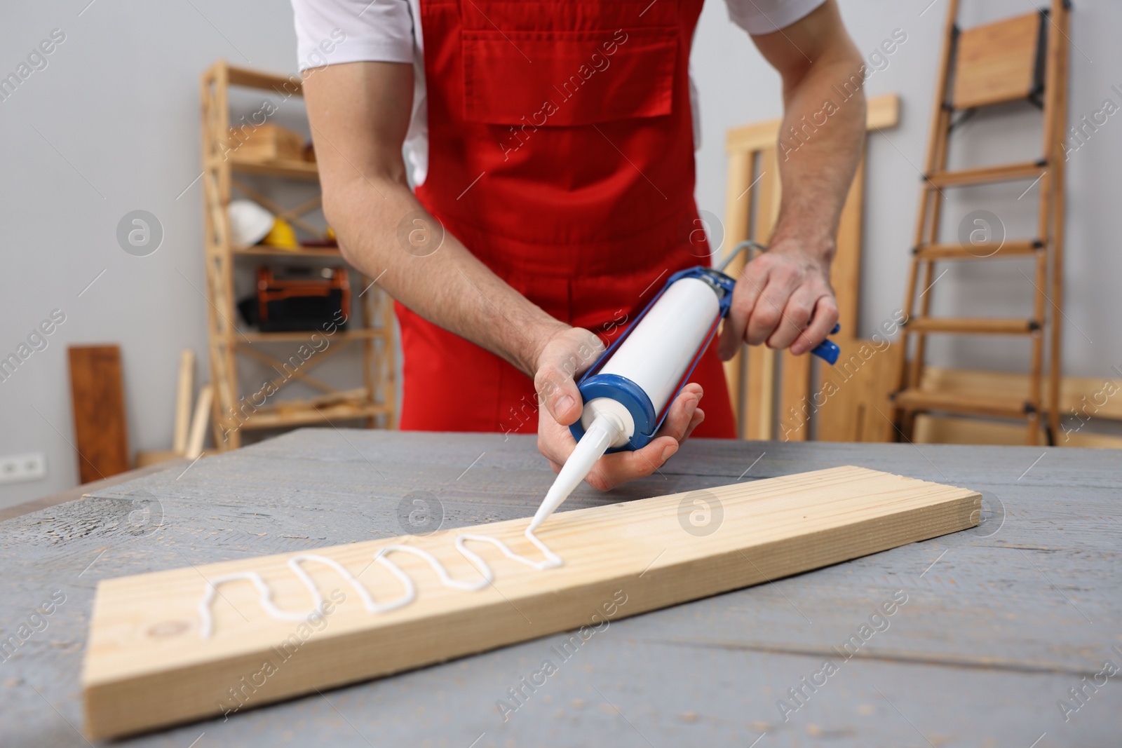 Photo of Worker with caulking gun glueing wooden plank indoors, closeup