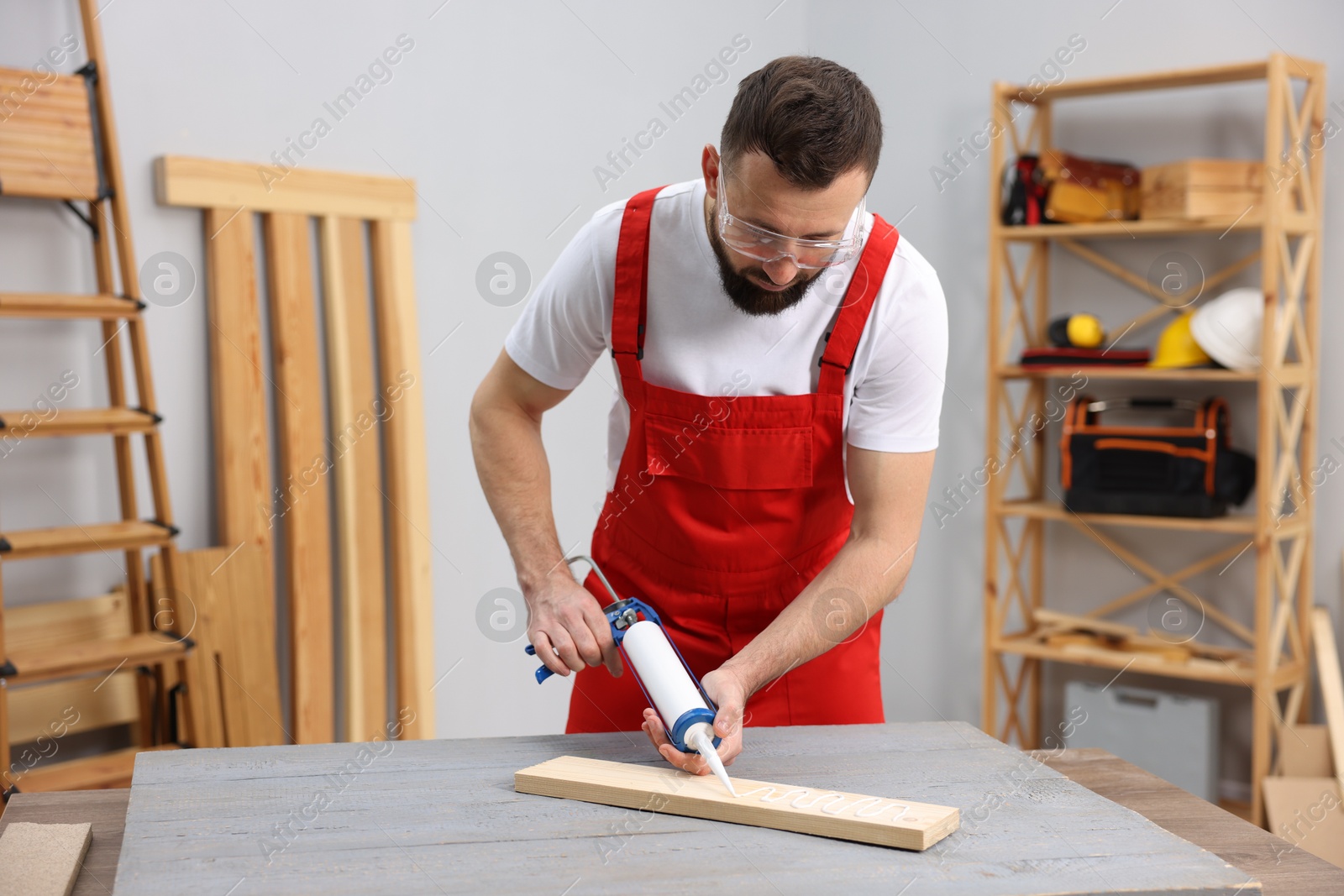 Photo of Worker with caulking gun glueing wooden plank indoors