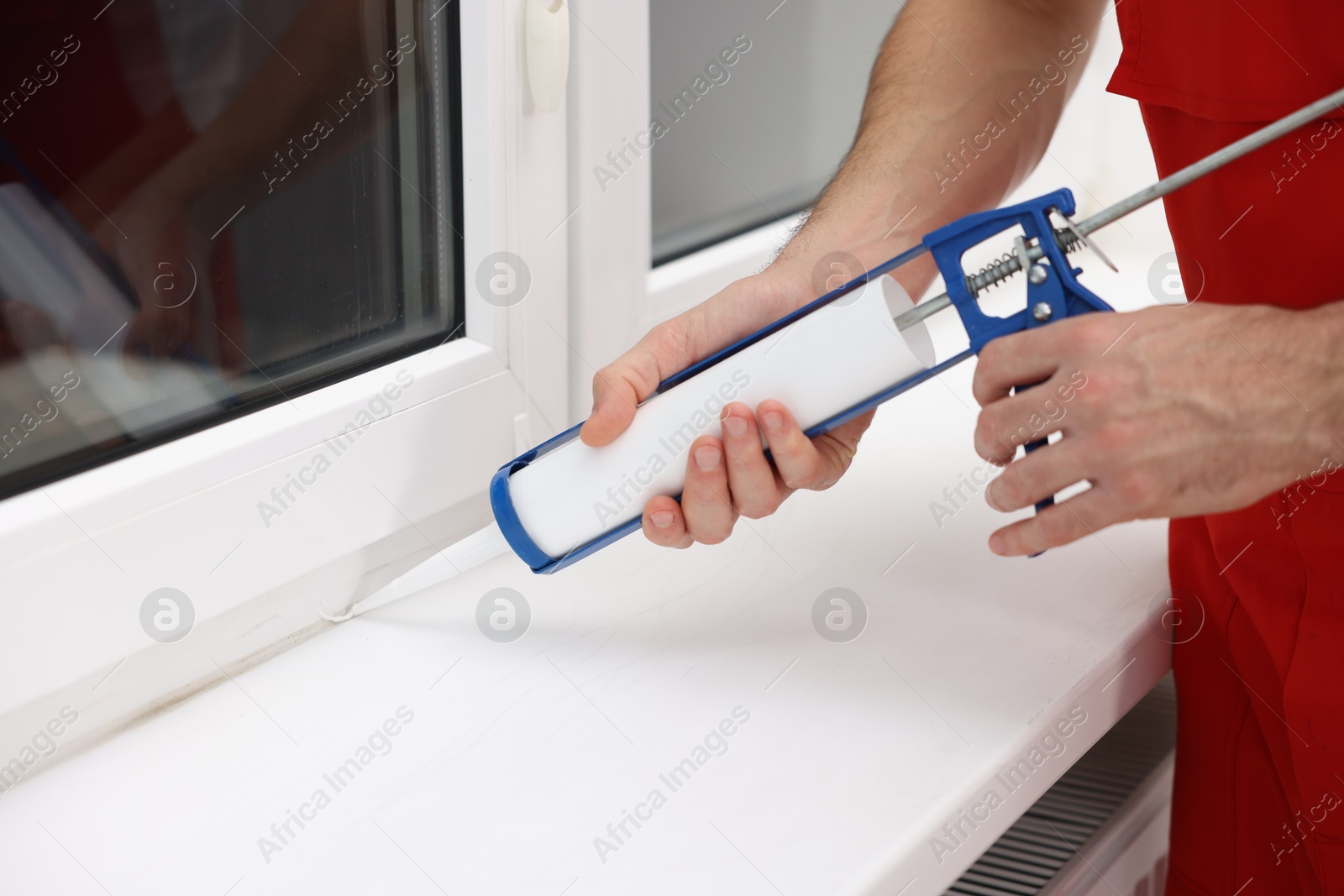 Photo of Worker with caulking gun sealing window indoors, closeup