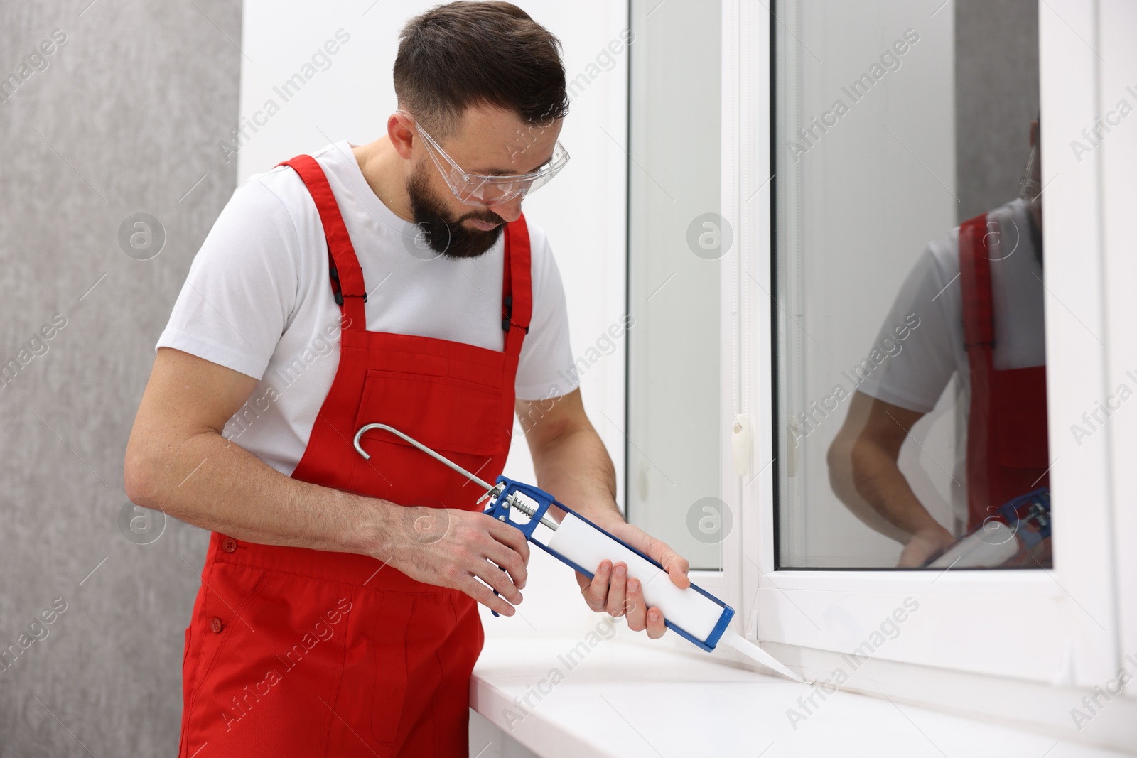 Photo of Worker with caulking gun sealing window indoors