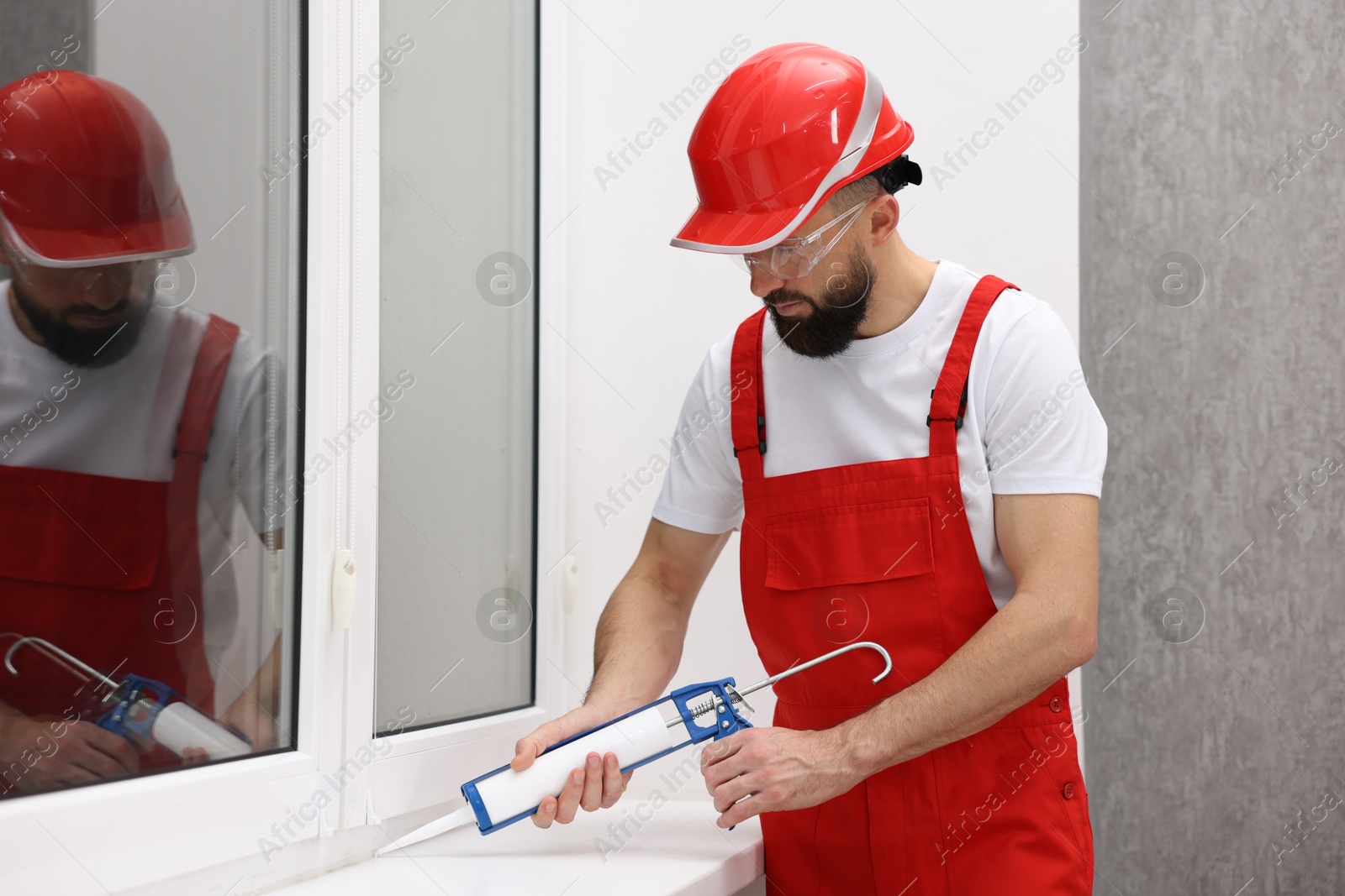 Photo of Worker with caulking gun sealing window indoors