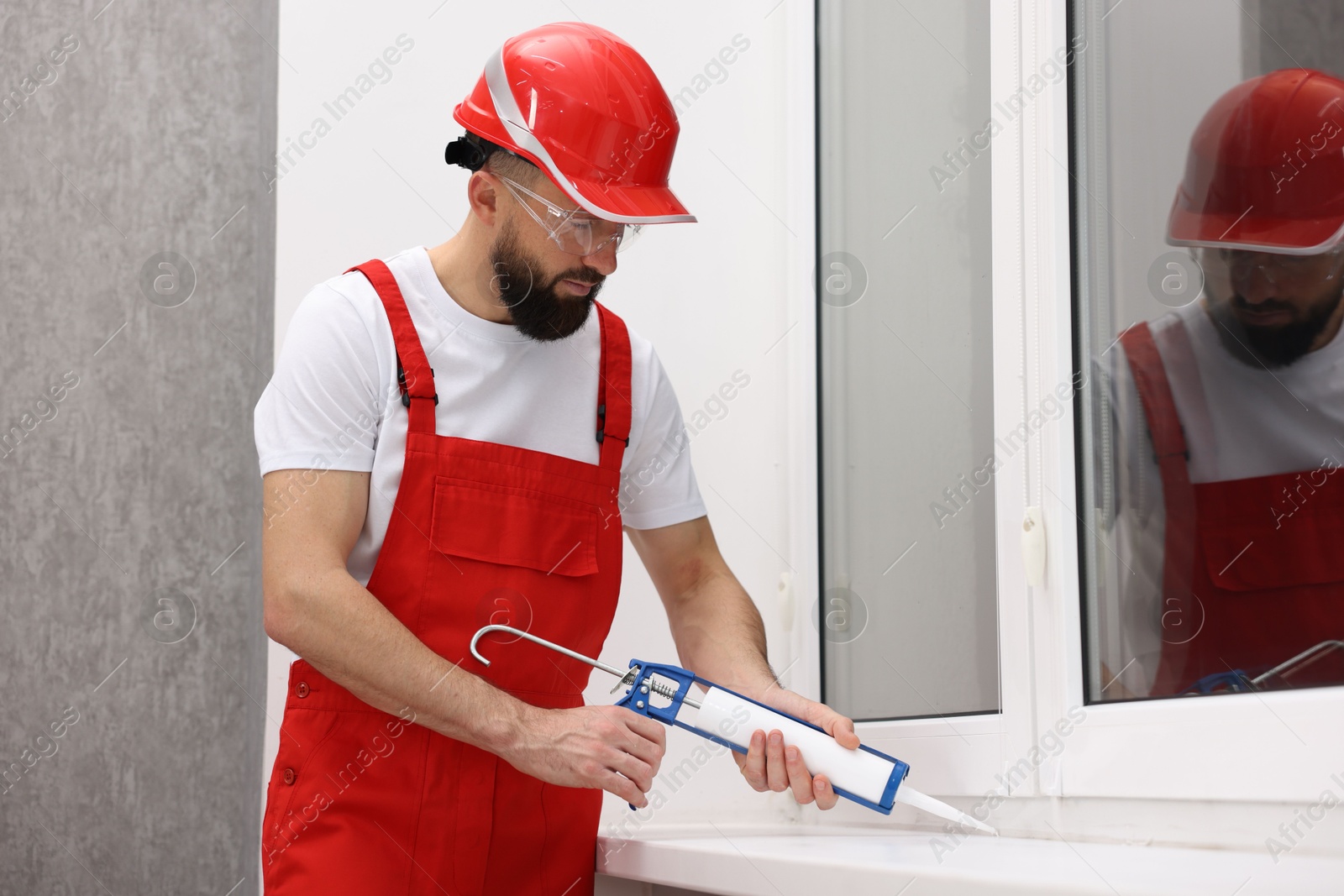 Photo of Worker with caulking gun sealing window indoors