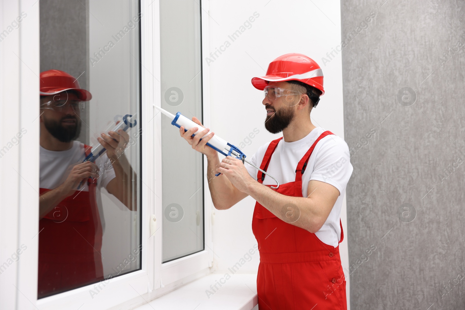 Photo of Worker with caulking gun sealing window indoors