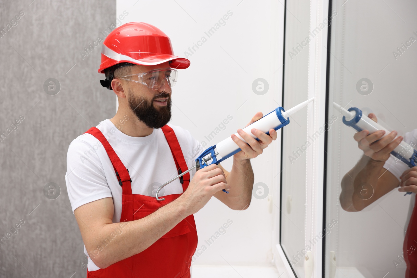 Photo of Worker with caulking gun sealing window indoors