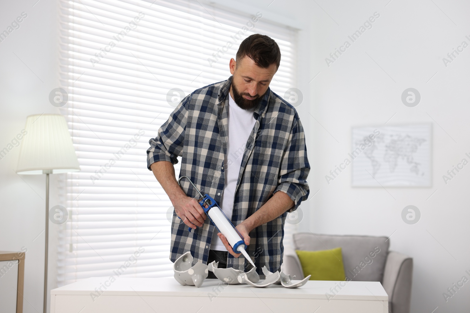 Photo of Man with caulking gun glueing pieces of ceramic piggy bank indoors