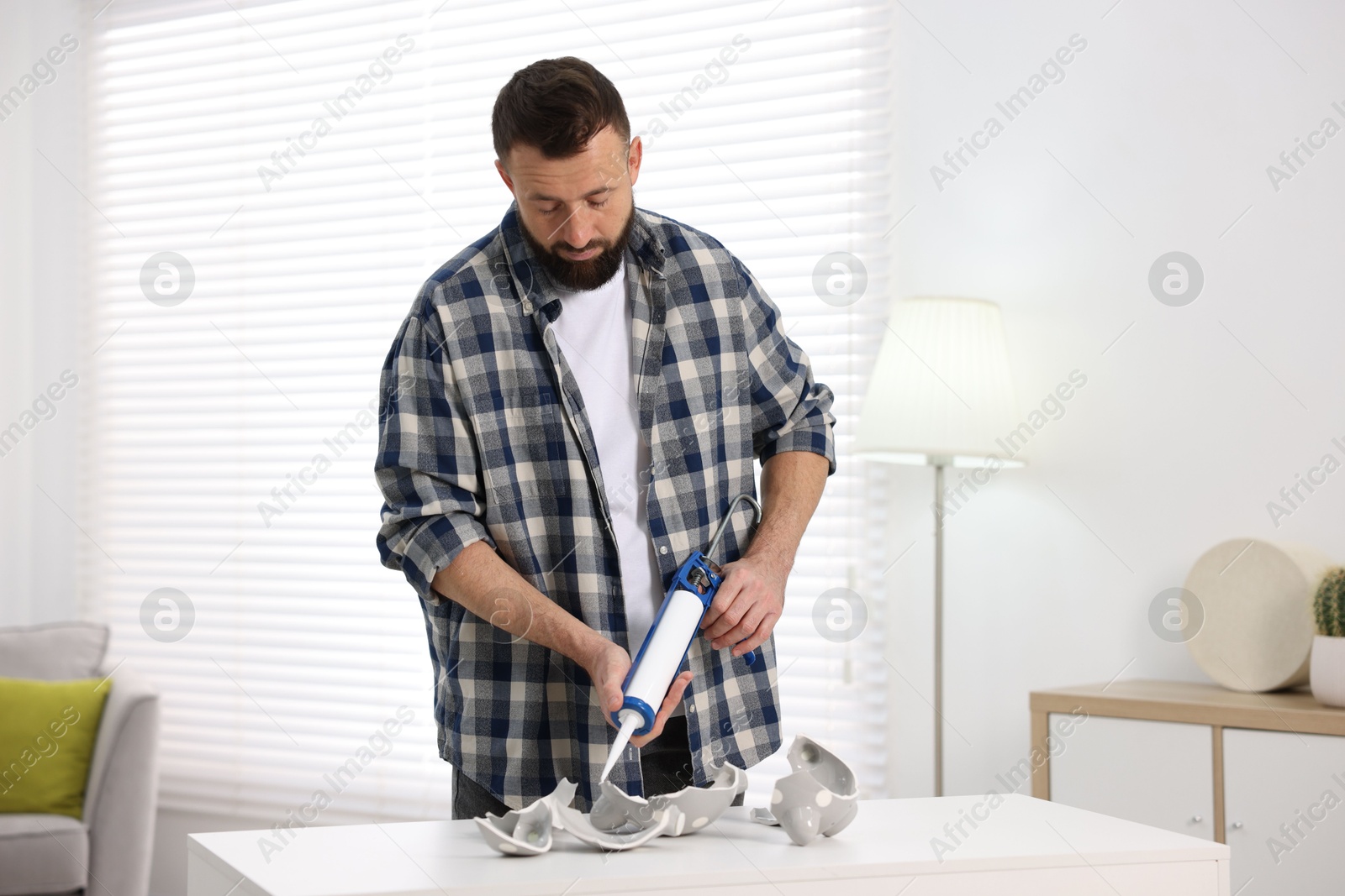 Photo of Man with caulking gun glueing pieces of ceramic piggy bank indoors