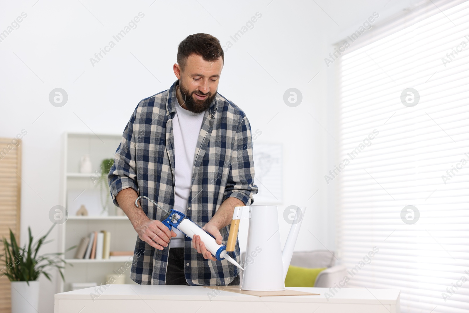 Photo of Man with caulking gun glueing watering can indoors