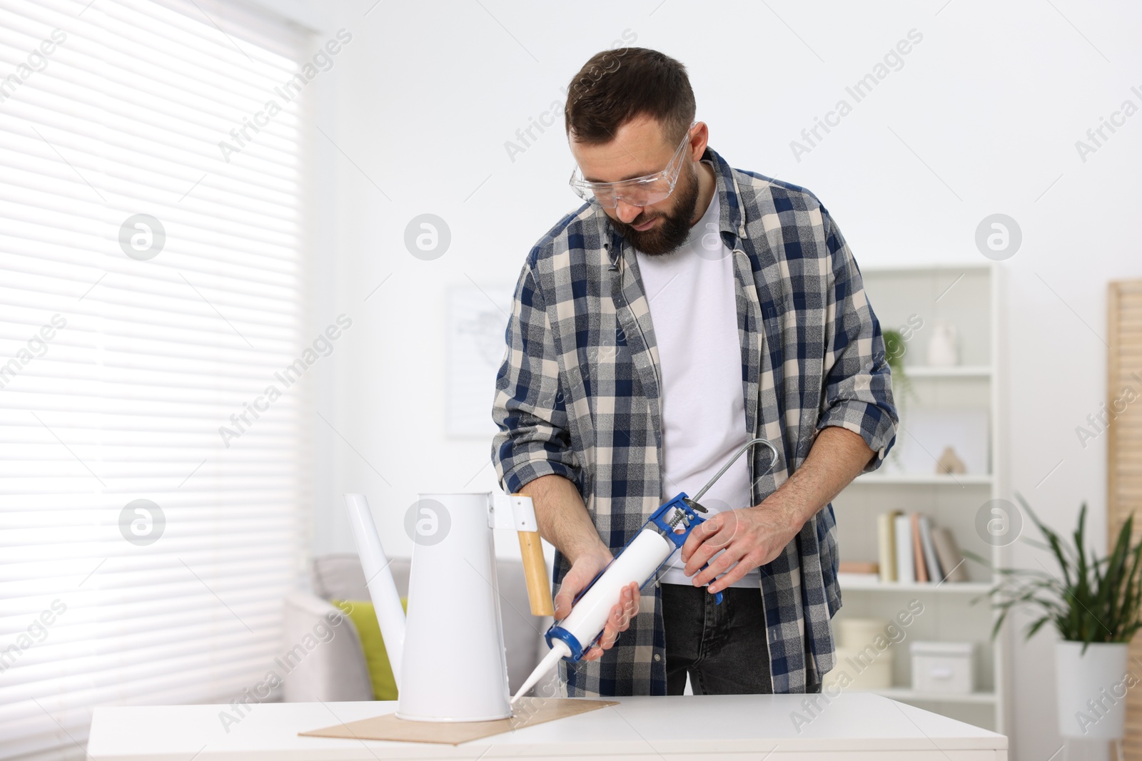 Photo of Man with caulking gun glueing watering can indoors