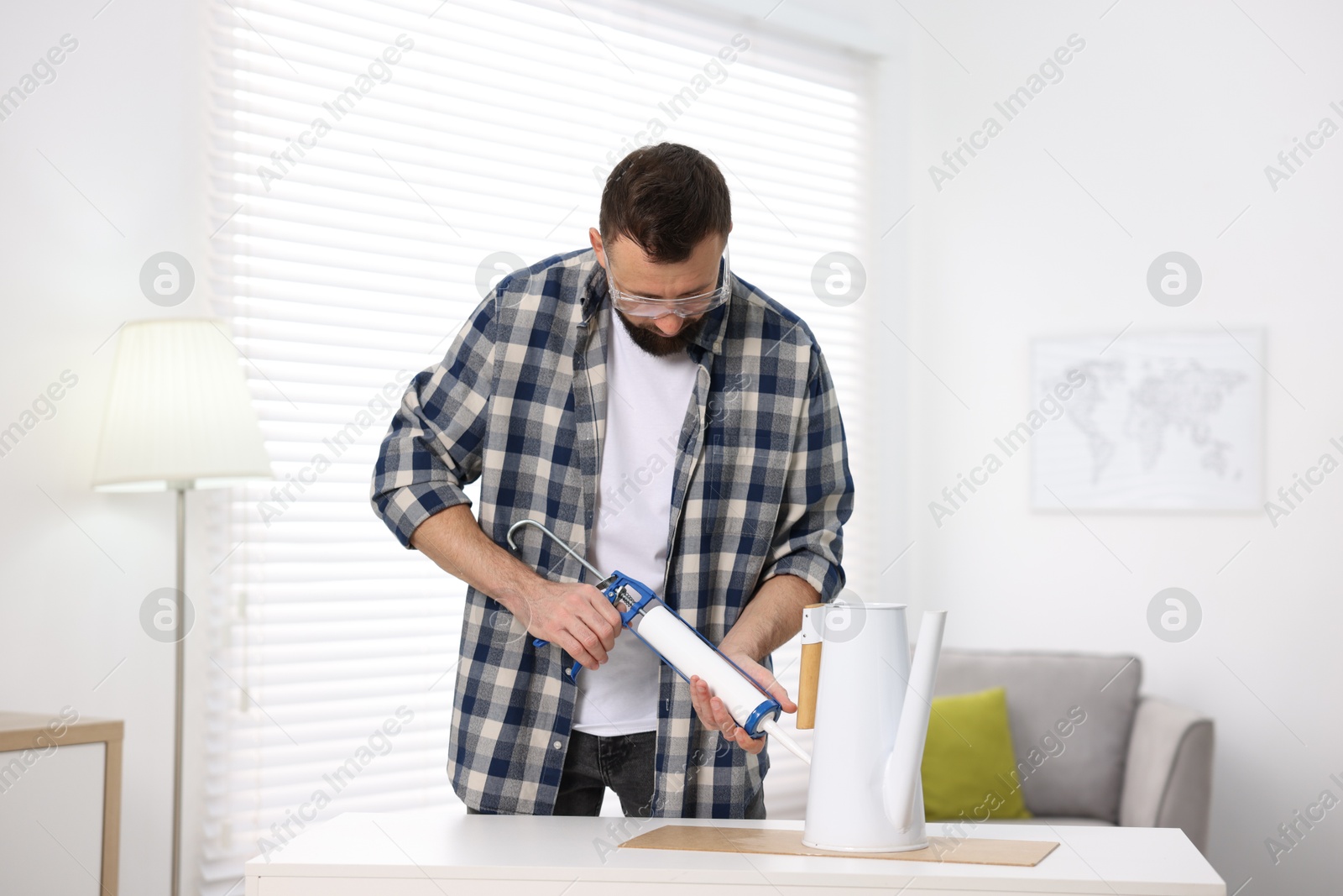 Photo of Man with caulking gun glueing watering can indoors