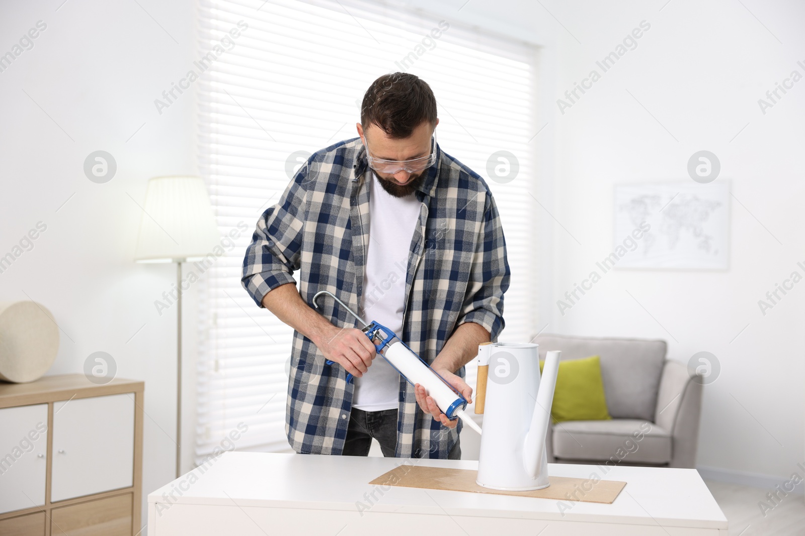 Photo of Man with caulking gun glueing watering can indoors