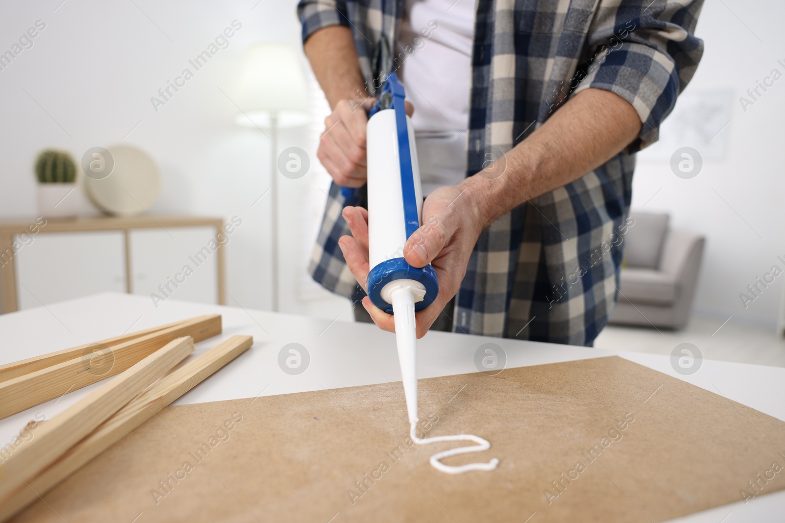 Photo of Man with caulking gun glueing plywood at white table indoors, closeup