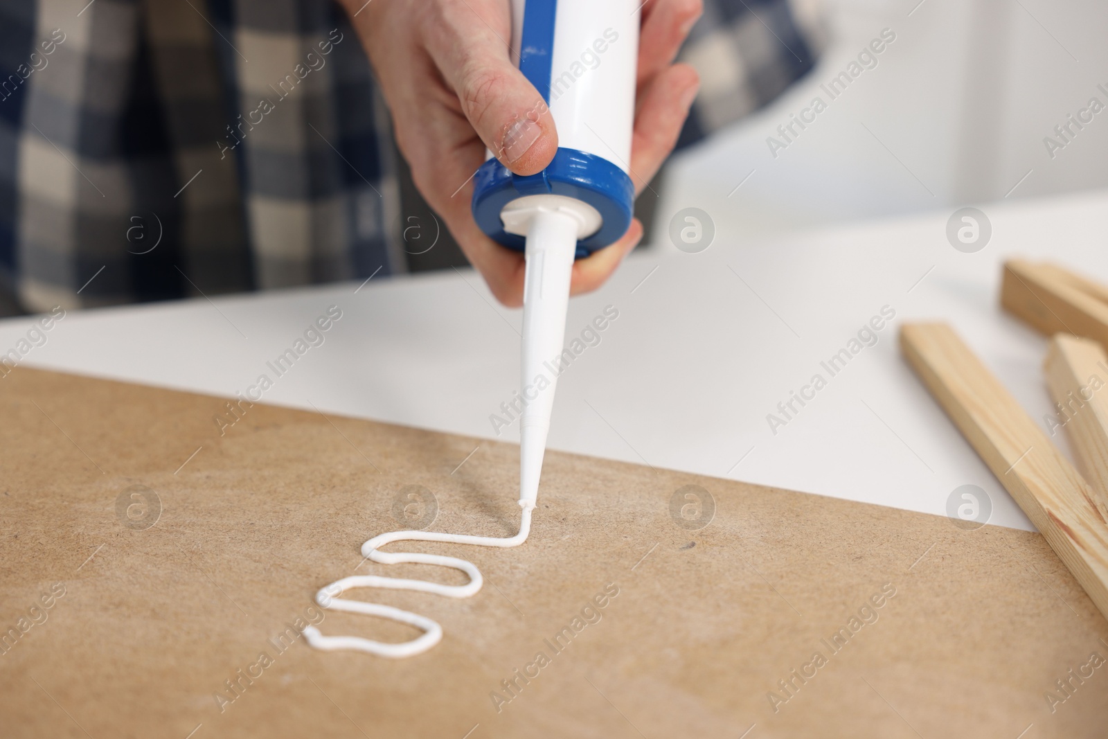 Photo of Man with caulking gun glueing plywood at white table, closeup