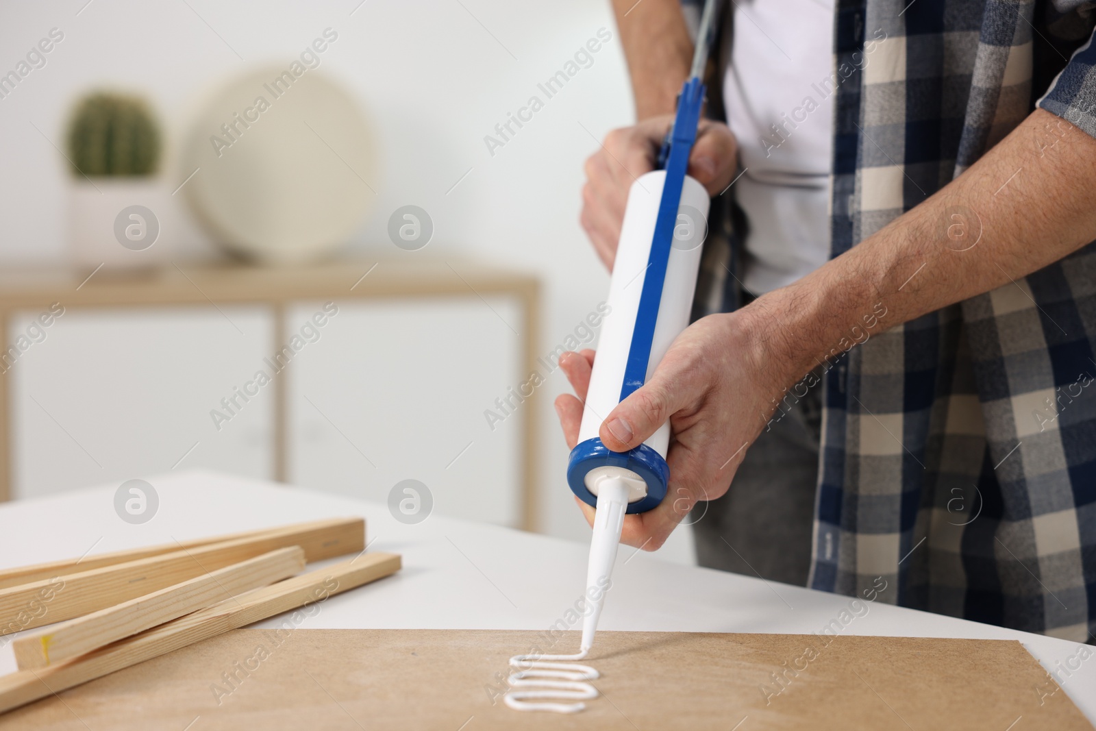 Photo of Man with caulking gun glueing plywood at white table indoors, closeup