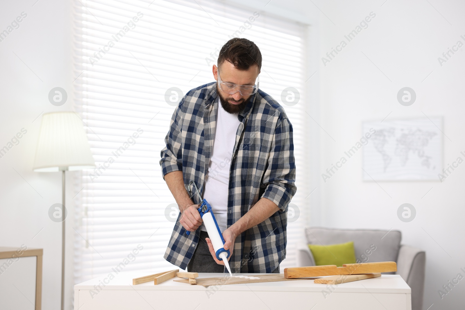 Photo of Man with caulking gun glueing plywood indoors