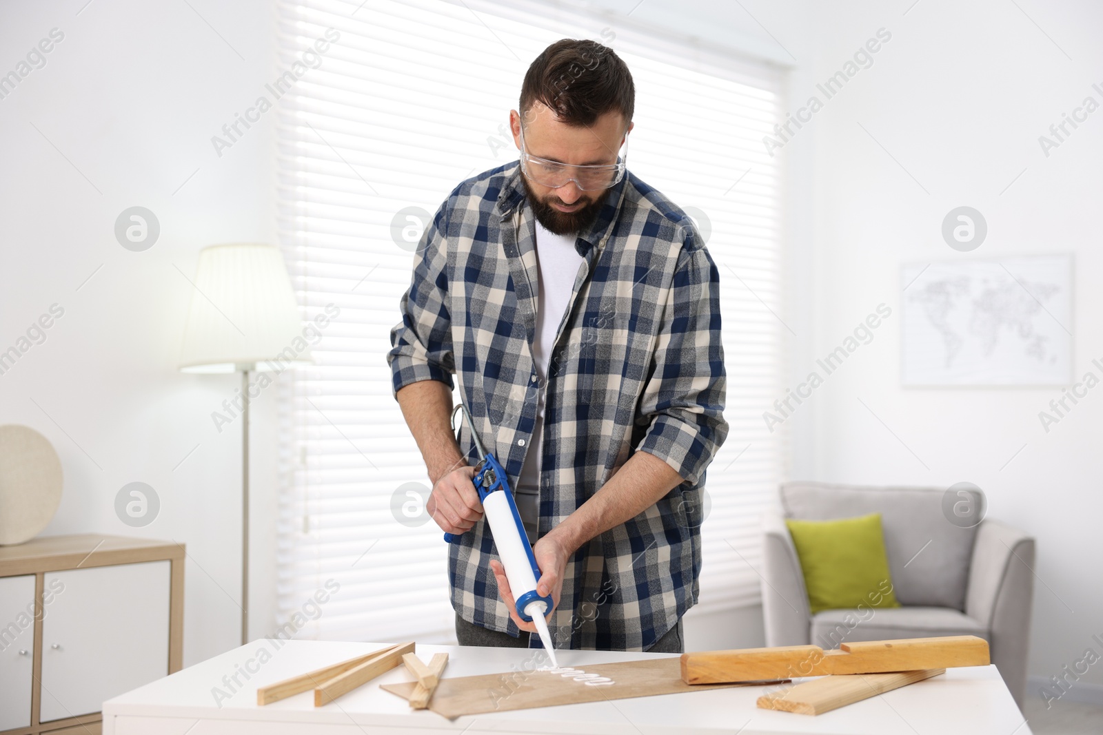 Photo of Man with caulking gun glueing plywood indoors