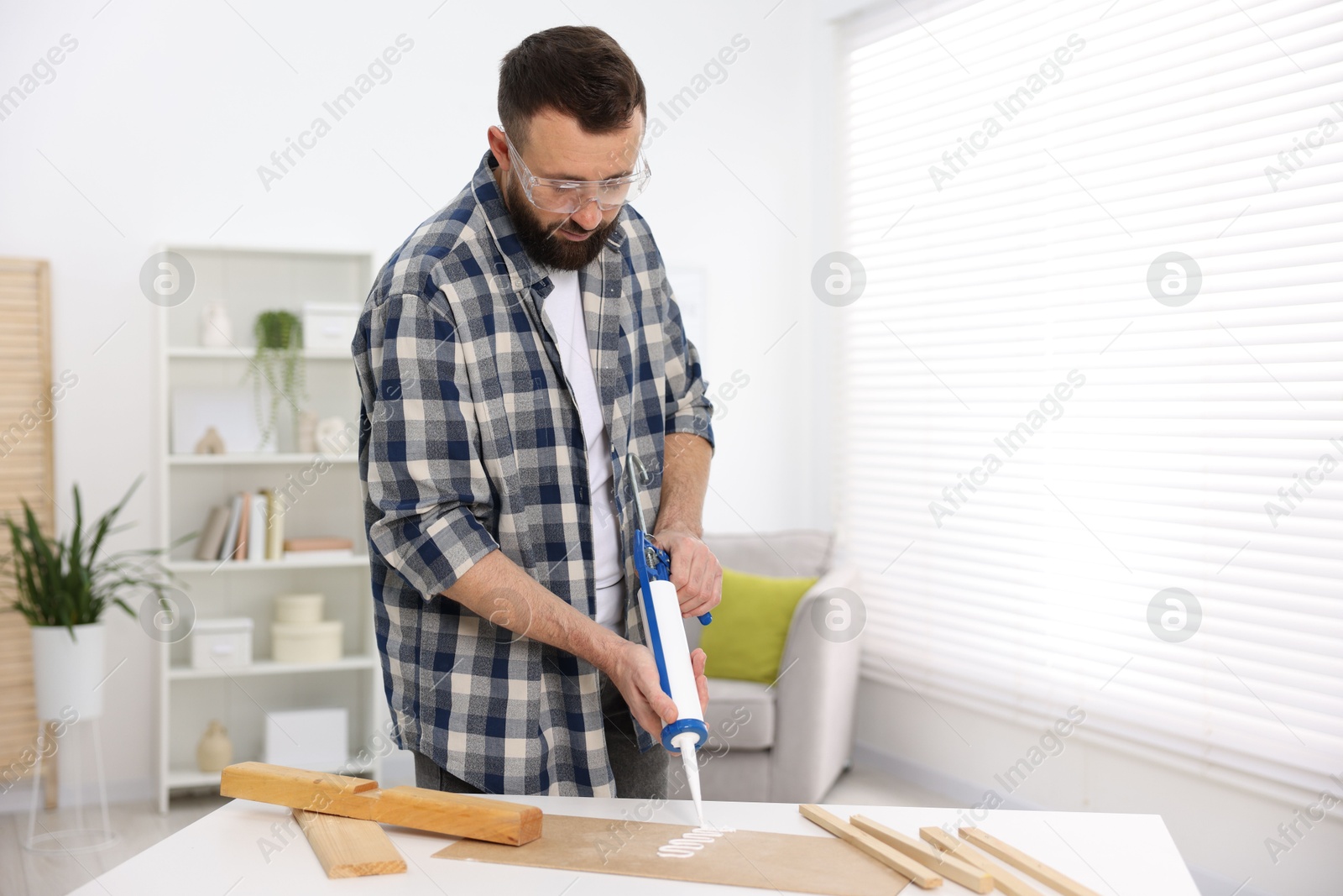 Photo of Man with caulking gun glueing plywood indoors