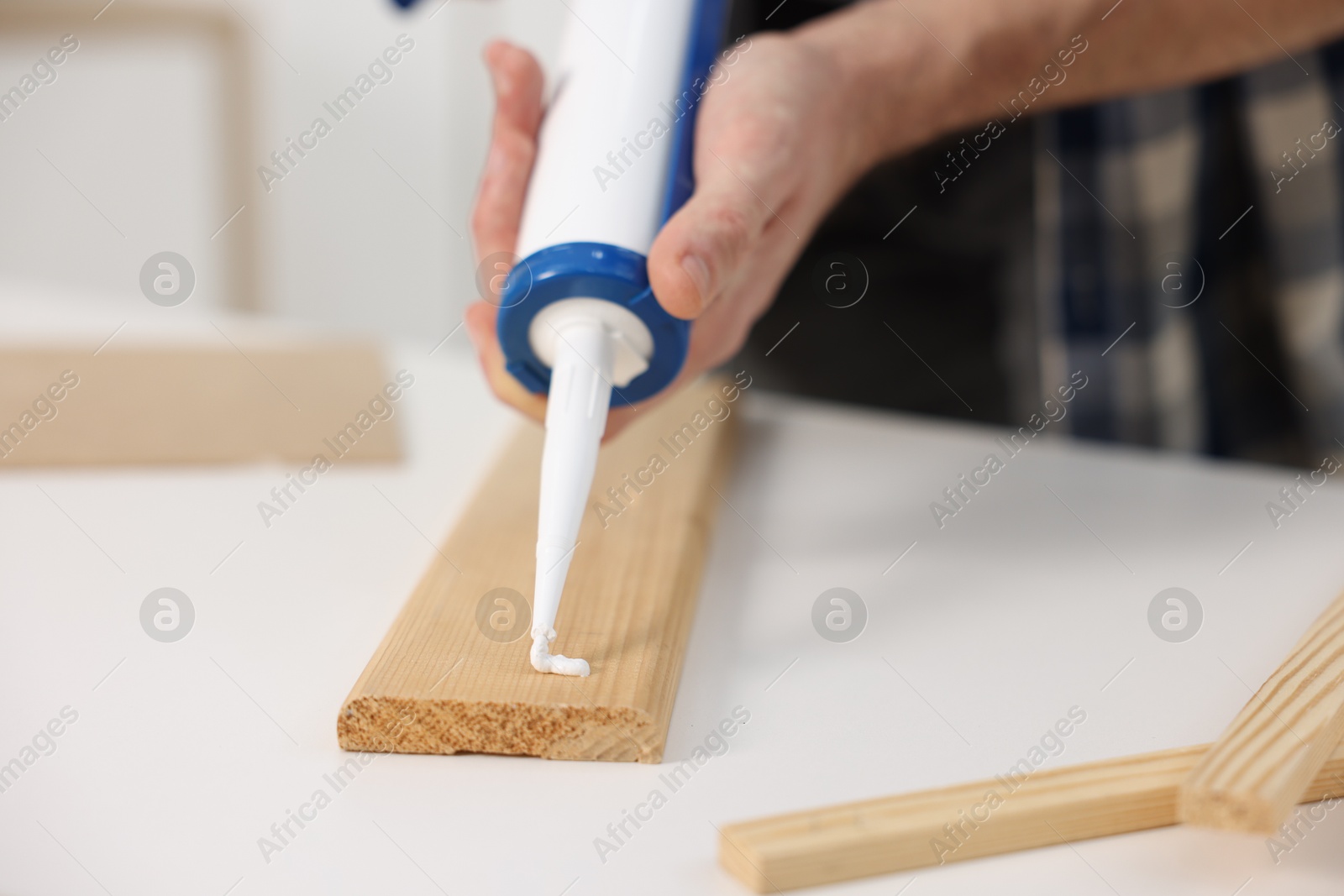 Photo of Man with caulking gun glueing wooden plank at white table, closeup