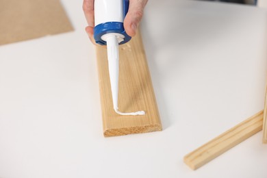 Photo of Man with caulking gun glueing wooden plank at white table, closeup