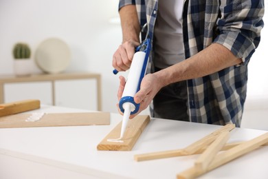 Photo of Man with caulking gun glueing wooden plank indoors, closeup